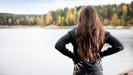 Kvinna som håller händerna på sin rygg vid en sjö. Foto: Mostphotos.