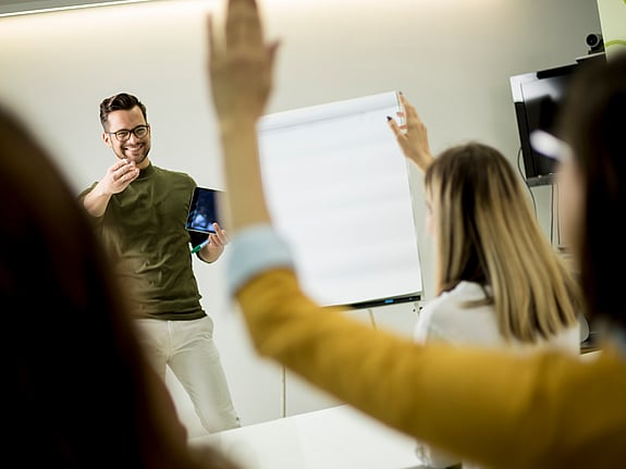 Student som räcker upp handen under en föreläsning. Foto: Mostphotos