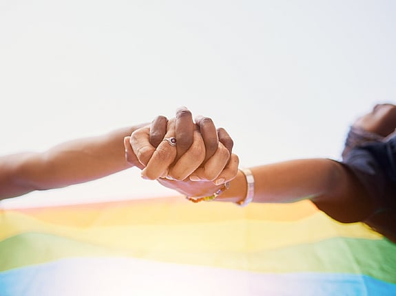 två personer som håller hand framför en regnbågsflagga. Foto: Mostphotos