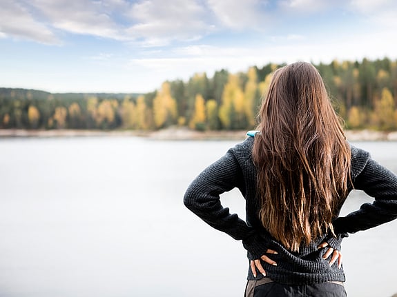 Kvinna som håller händerna på sin rygg vid en sjö. Foto: Mostphotos.